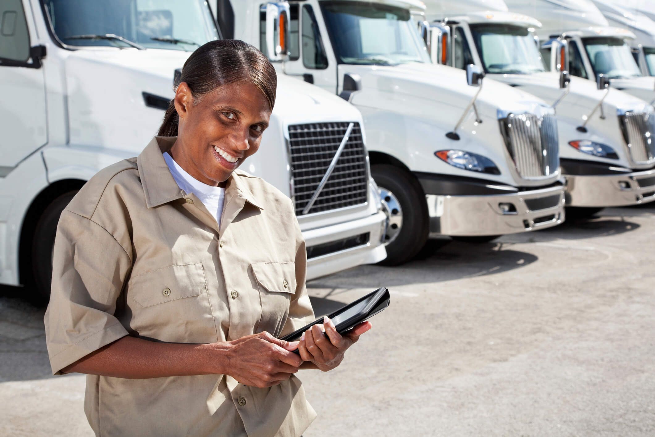 A fleet owner reviews fleet fuel card usage on a tablet in front of her fleet of trucks.