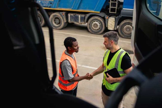 A fleet manager shakes hands with a truck driver on his team outside of his rig.