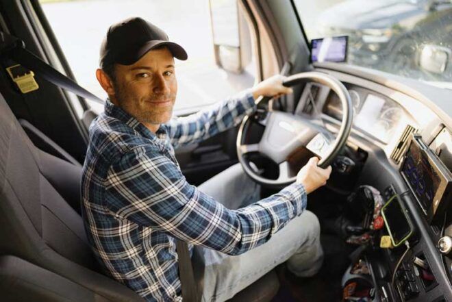A truck driver smiles from the cab of his semi truck.
