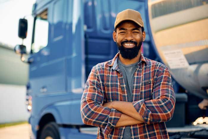 A happy truck driver stands outside his truck.